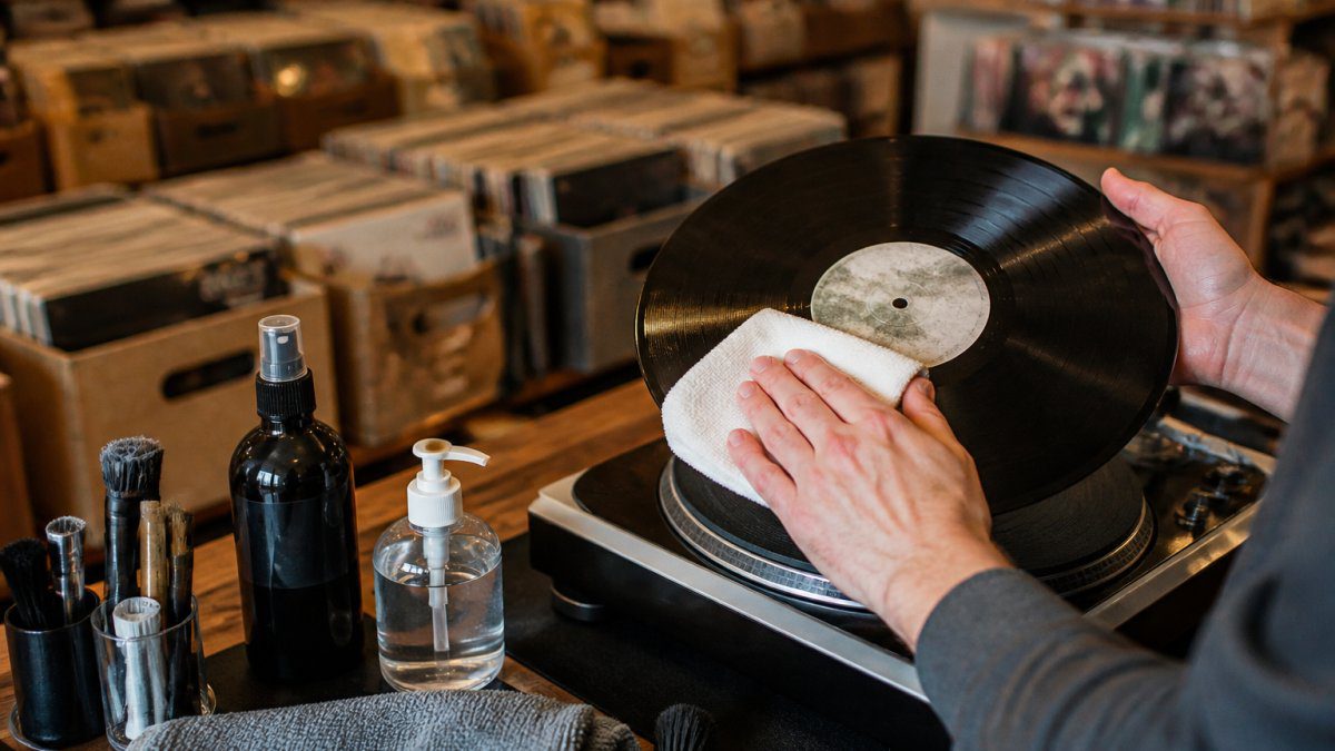 Hands carefully wiping a used vinyl record with a soft cloth near a turntable in a record store